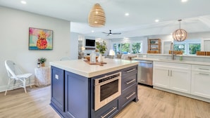 A modern kitchen with a central island, white cabinetry, and a large window providing a view of greenery. - 4 Cannon Row at The Sea Pines Resort (Hilton Head Island)