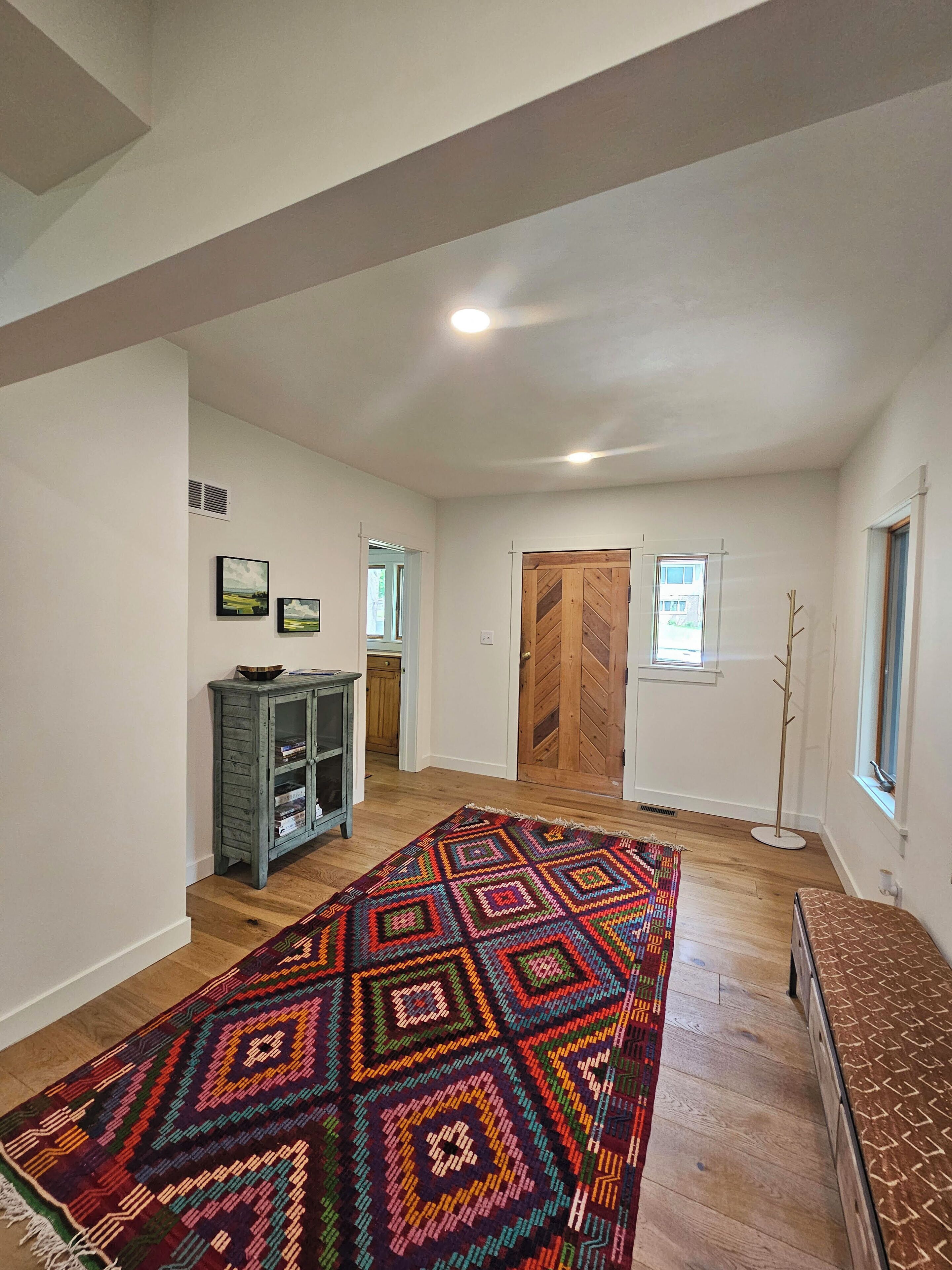 A spacious room with a large colorful rug, wooden flooring, a cabinet, and a bench.