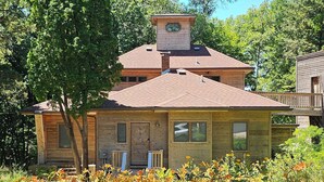 A two-story house with a visible chimney, surrounded by lush greenery and flowering plants.