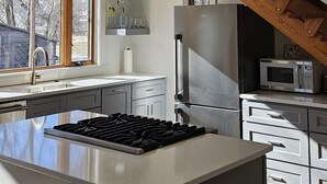 A modern kitchen with a large island, stainless steel appliances, and a wooden ceiling.