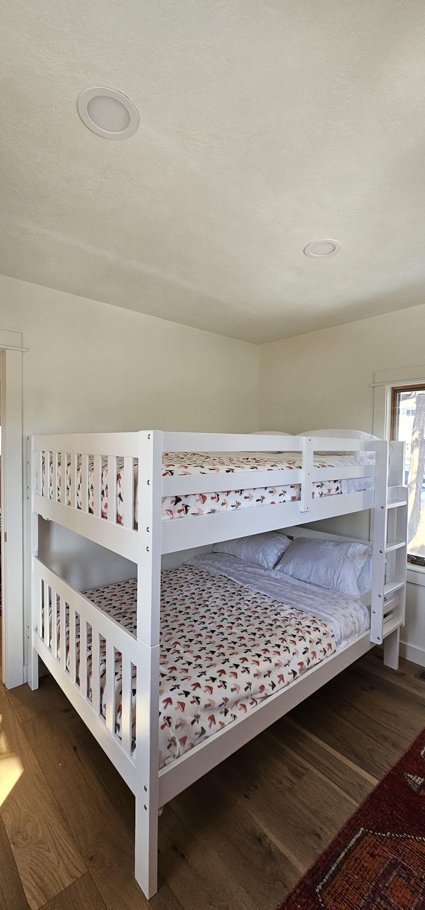 Una cama litera con una colcha estampada, una pared blanca y un suelo de madera.
