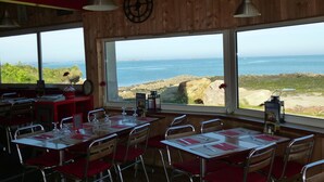 Een restaurant met gedekte tafels, grote ramen met uitzicht op zee en houten wanden.