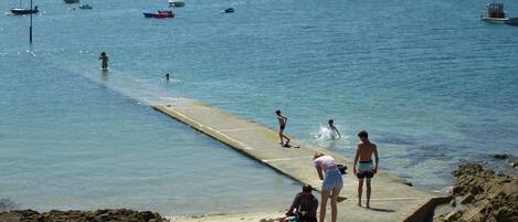 A coastal scene with a pier extending into the water, surrounded by boats and people engaging in various activities.