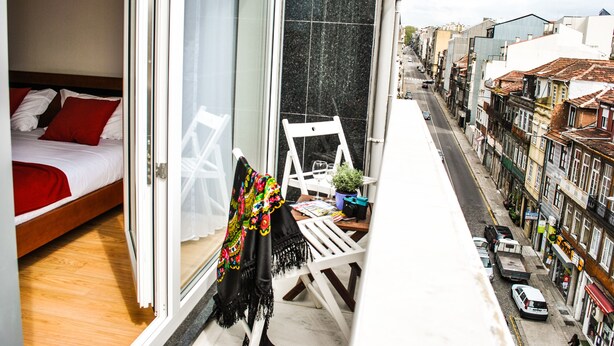 Un balcon avec un lit, une chaise et une table agrémentée d’une plante.