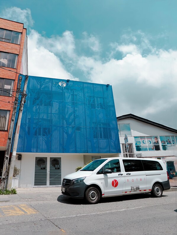 A white van parked in front of a building with a blue perforated facade and a sign indicating a hotel.