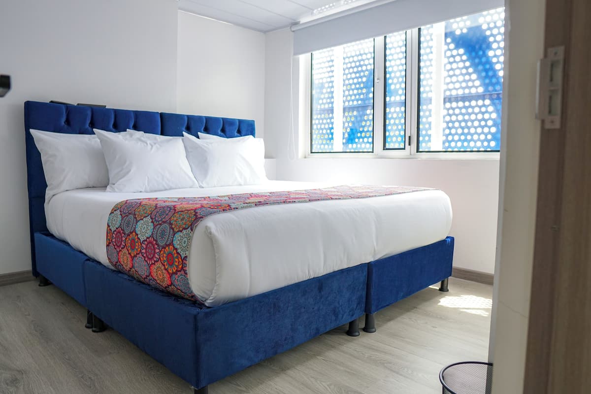 Une chambre moderne avec un lit recouvert d’un tissu bleu, du linge de lit blanc et un plaid coloré.