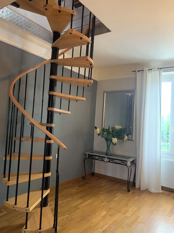 A spiral staircase with wooden steps and black railings, a wooden console table with a vase of flowers, and a large mirror on the wall.