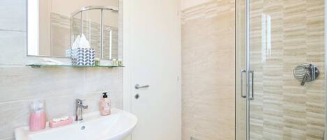 A modern bathroom with a glass shower enclosure, a white sink with pink accessories, and a mirror above the sink.