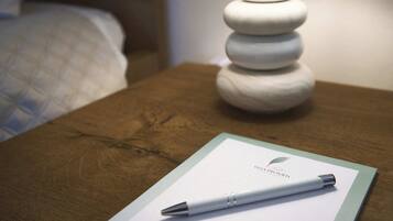A neatly made bed with a pillow, a bedside table with a pen and a card, and a stack of white objects on the table.