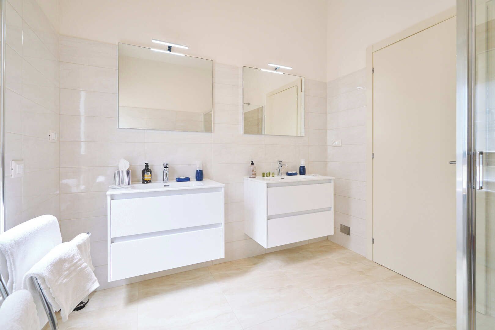 A modern bathroom with two sinks, large mirrors, and a glass shower enclosure.