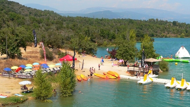 A beach with sun loungers, umbrellas, and a dock with boats.