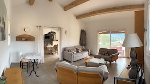 A spacious living area with a sofa, chairs, a dining table, and a balcony with a view.