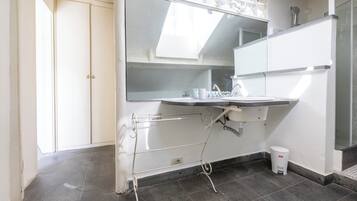 A modern bathroom with a white sink, mirror, and towel rack. There is a small trash bin and a shower area visible.