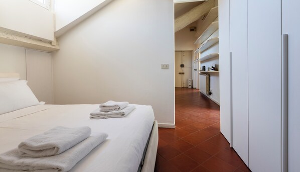 A hotel room with a neatly made bed, a radiator, and a hallway leading to a bathroom. - Italianway - Vigevano 7 (Milan)