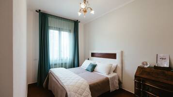 Une chambre à coucher bien rangée, avec un lit, une commode et un lustre.