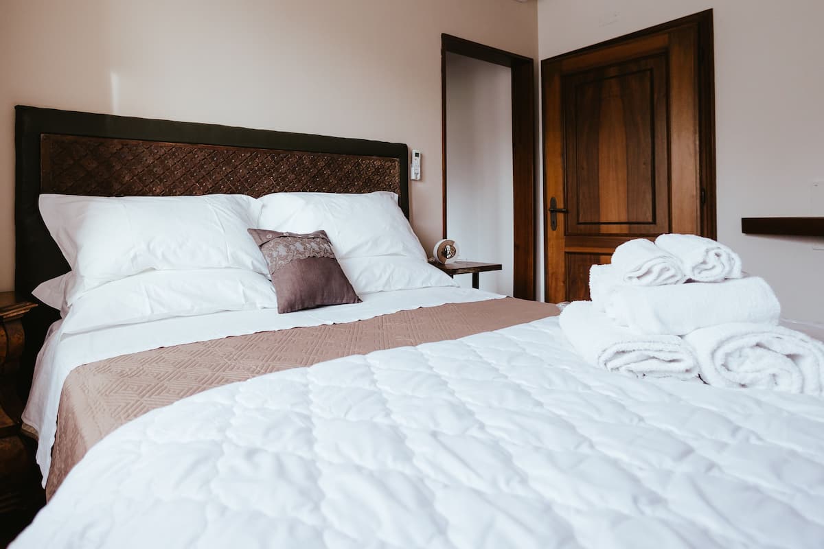 A neatly made bed with white linens and a brown throw blanket, a wooden headboard, and a wooden door in the background.