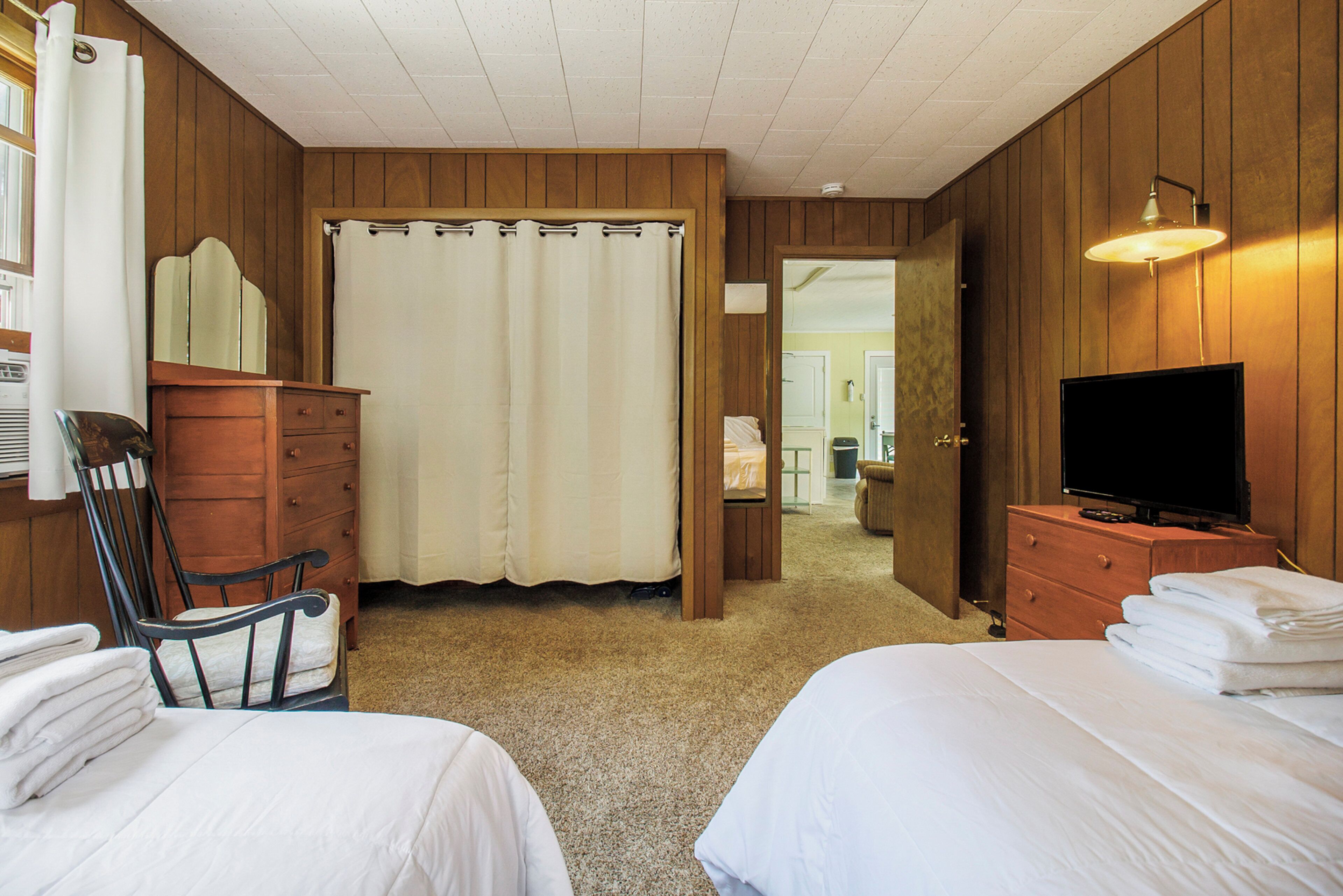 Een hotelkamer met twee bedden, een houten dressoir, een televisie en een spiegel.