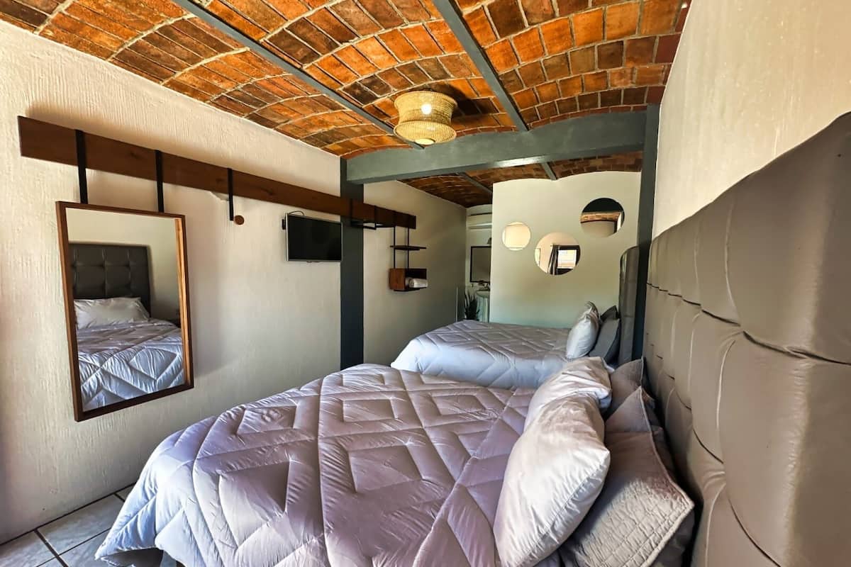 A bedroom with a brick ceiling, a large bed with a headboard, a mirror, and a television on the wall.