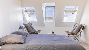 A bedroom with a large bed, two wicker chairs, a small table, and a skylight window.