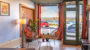 A room with a brick wall, wicker chairs, a small table with a red cup, and a view of a parking lot through a glass door.