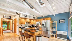 A modern kitchen with wooden cabinets, a stainless steel refrigerator, and a large island with bar stools. - Serene Home with Ocean View   (Juneau)