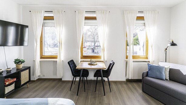 A modern living room with a dining table, two chairs, a sofa, and a TV.