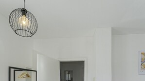 A modern living room with a wooden floor, a grey sofa, a small side table, and a hanging light fixture.