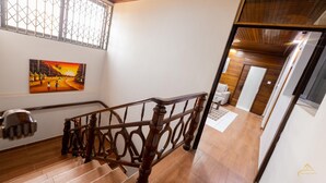 Uma escadaria com guarda-corpos de madeira, um quadro na parede e vista para um quarto adjacente.