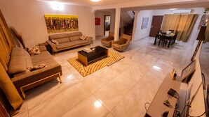 Uma sala de estar ampla com sofá, poltronas, mesa de centro e um espaço de jantar com mesa e cadeiras.
