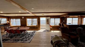 A spacious room with a large dining table, multiple chairs, and a view of a body of water through large windows.