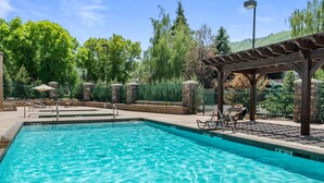 A clear swimming pool with lounge chairs and a pergola.