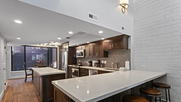A modern kitchen with a large island, dark wooden cabinets, and a white countertop.