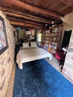 Une chambre avec un grand lit, une bibliothèque et un mur en pierre.