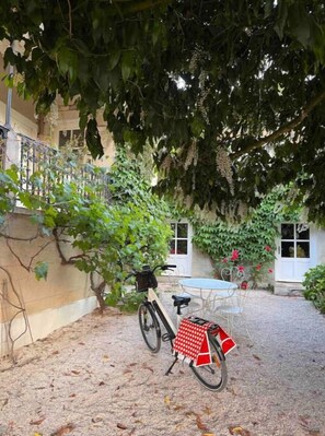 Un vélo est garé sous un arbre dans une cour où se trouvent une table et des chaises.