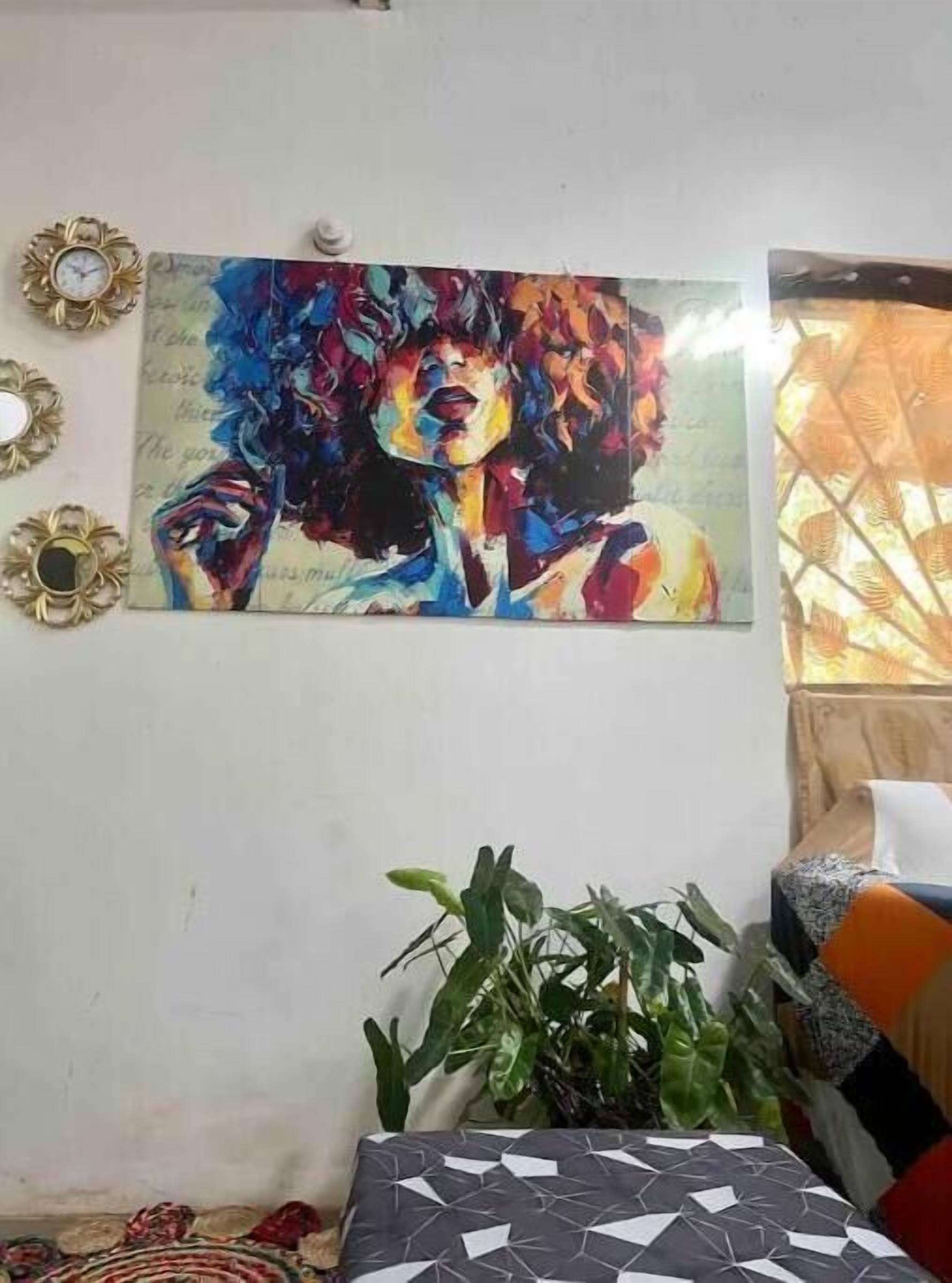 A room with a colorful abstract painting on the wall, a potted plant, and a patterned sofa.