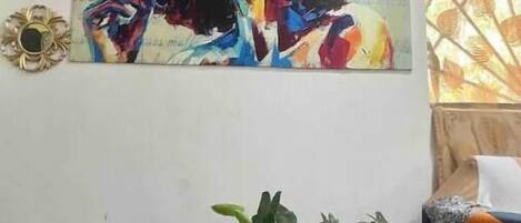 A room with a colorful abstract painting on the wall, a potted plant, and a patterned sofa.
