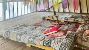 A room with a thatched roof, a bed with patterned bedding, and a view of greenery outside.