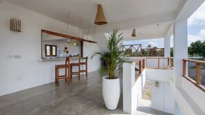Zona d'estar àmplia amb menjador, una gran planta en test i vista a l'exterior.