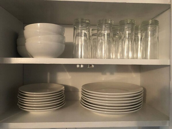 A kitchen shelf with stacked white plates and clear glass jars.