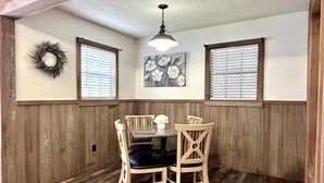 A dining area with a wooden bench, two chairs, a table, and a pendant light. - Doc's Cottage - A-Frame in Piggott, AR (Piggott)