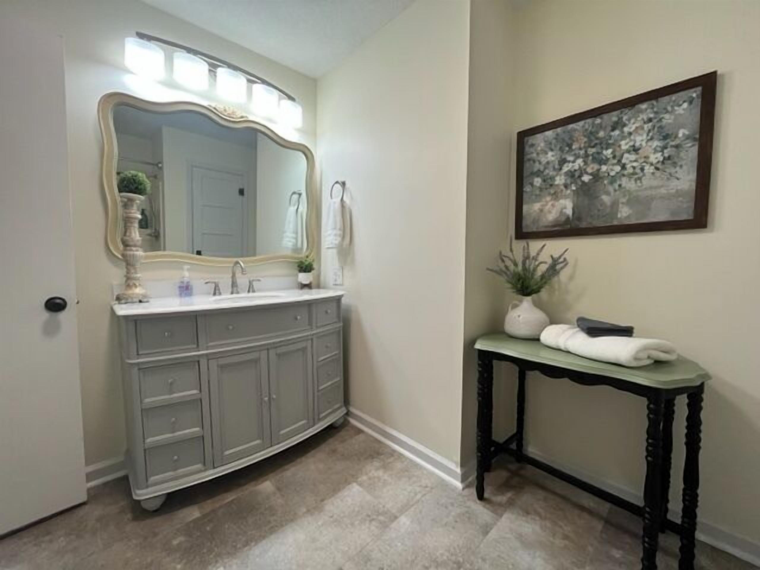 A bathroom with a vanity, a large mirror, a sink, and a small table with towels.