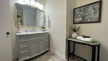 A bathroom with a vanity, a large mirror, a sink, and a small table with towels.