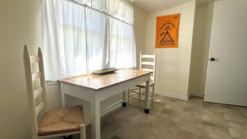 Un comedor con una mesa y dos sillas, una ventana con cortinas translúcidas y una puerta al fondo.