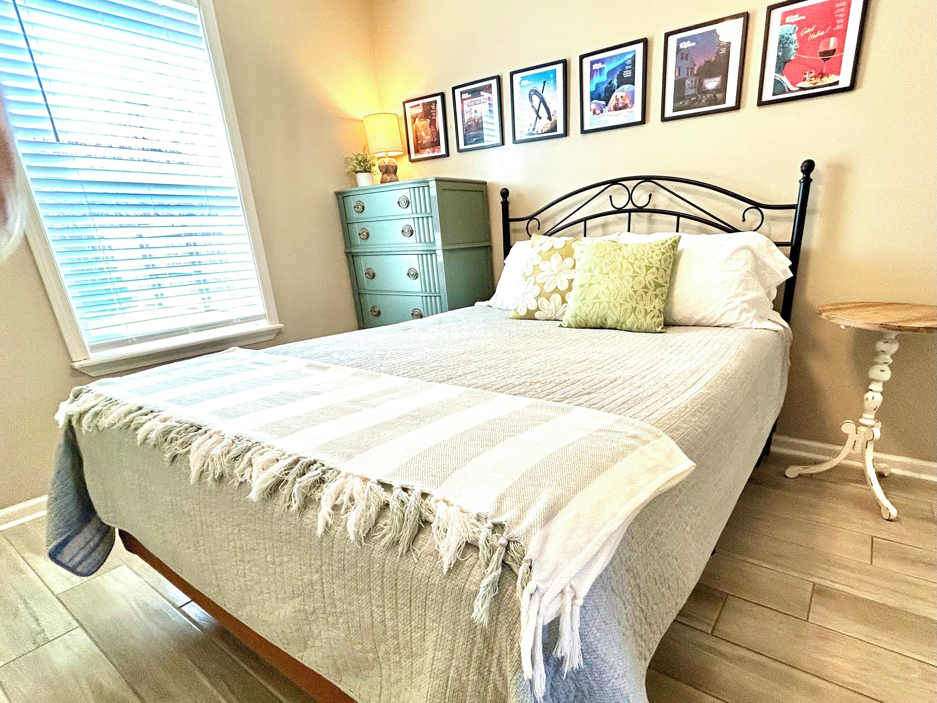 Une chambre à coucher avec un lit, une commode, une lampe et des tableaux encadrés accrochés au mur.