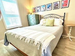 Un dormitorio con cama, cómoda, lámpara y cuadros en la pared.