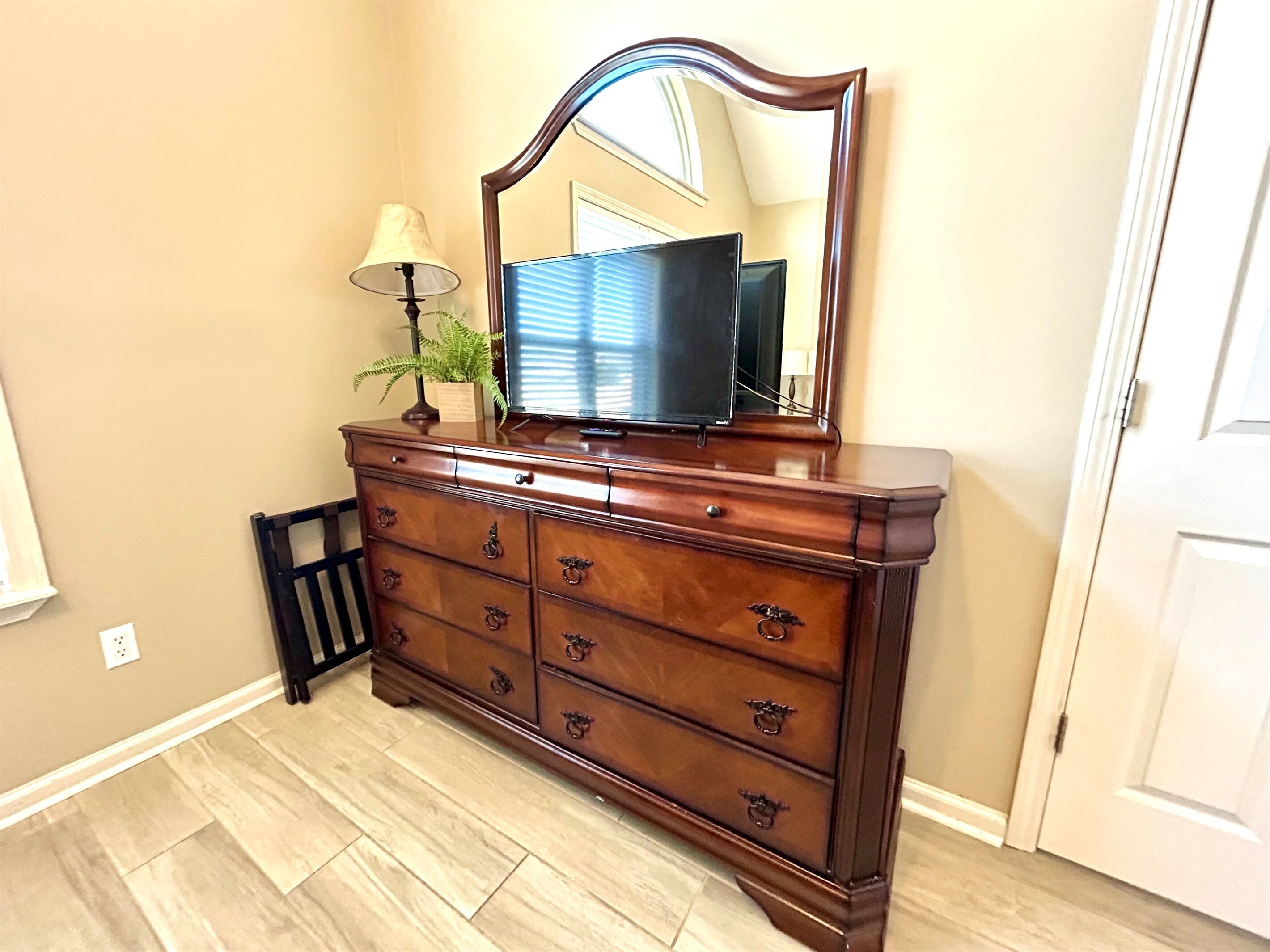 A wooden dresser with a mirror and a television, a lamp, and a plant.