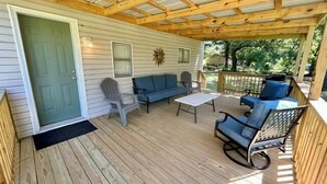 A covered porch with wooden flooring, a green door, and outdoor seating including a sofa, chairs, and a table.