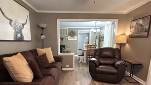 A living room with a brown leather sofa, a leather armchair, and a dining area in the background.