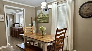 A dining room with a wooden table, chairs, a vase with flowers, a clock, and a painting on the wall.