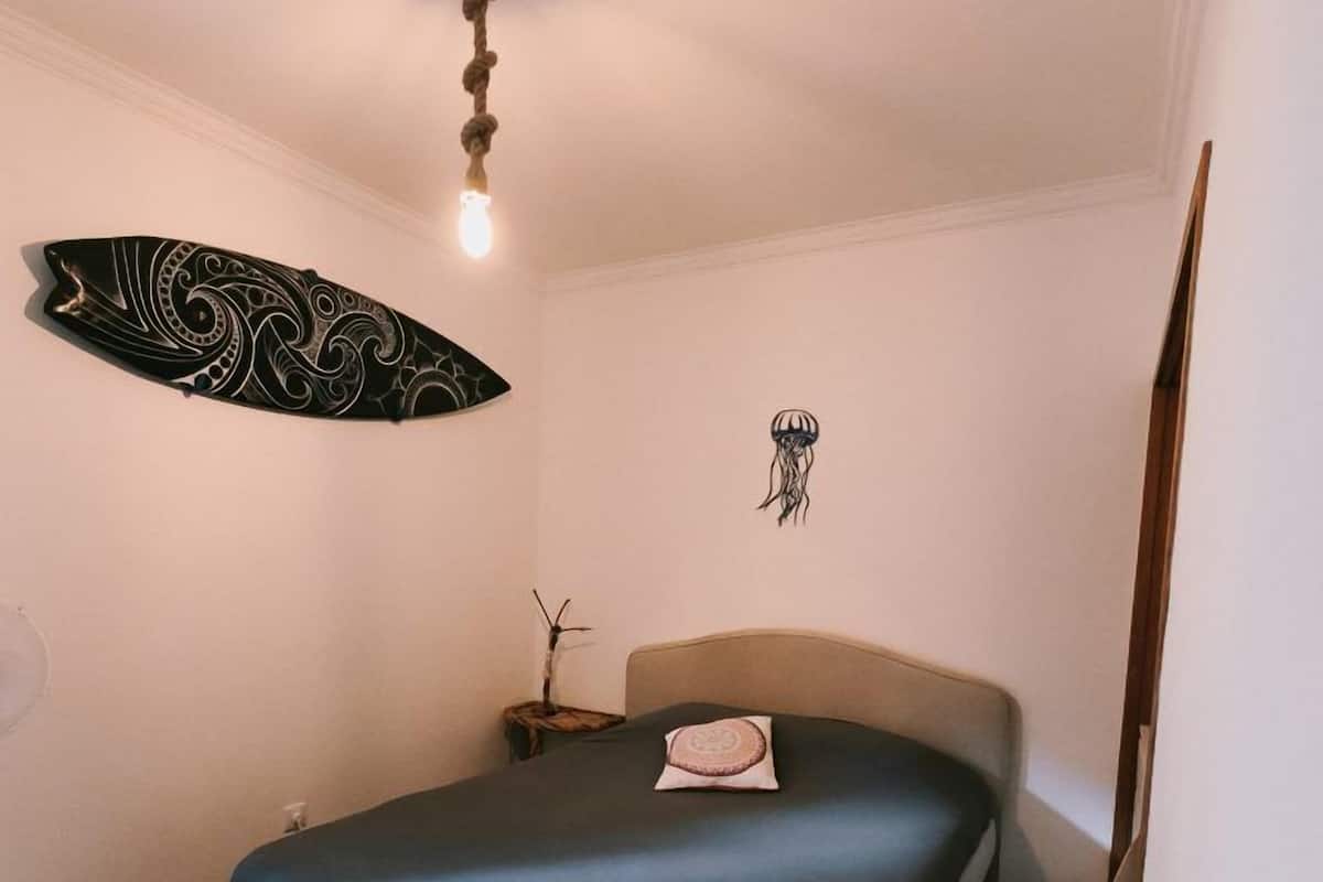 A bedroom with a bed, a wall decoration, a ceiling light, and a wooden floor.